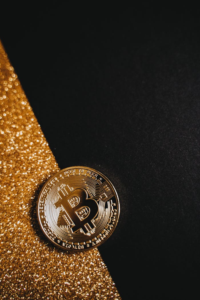 Close-up of a shiny Bitcoin coin on a black surface, accented by sparkling gold glitter.